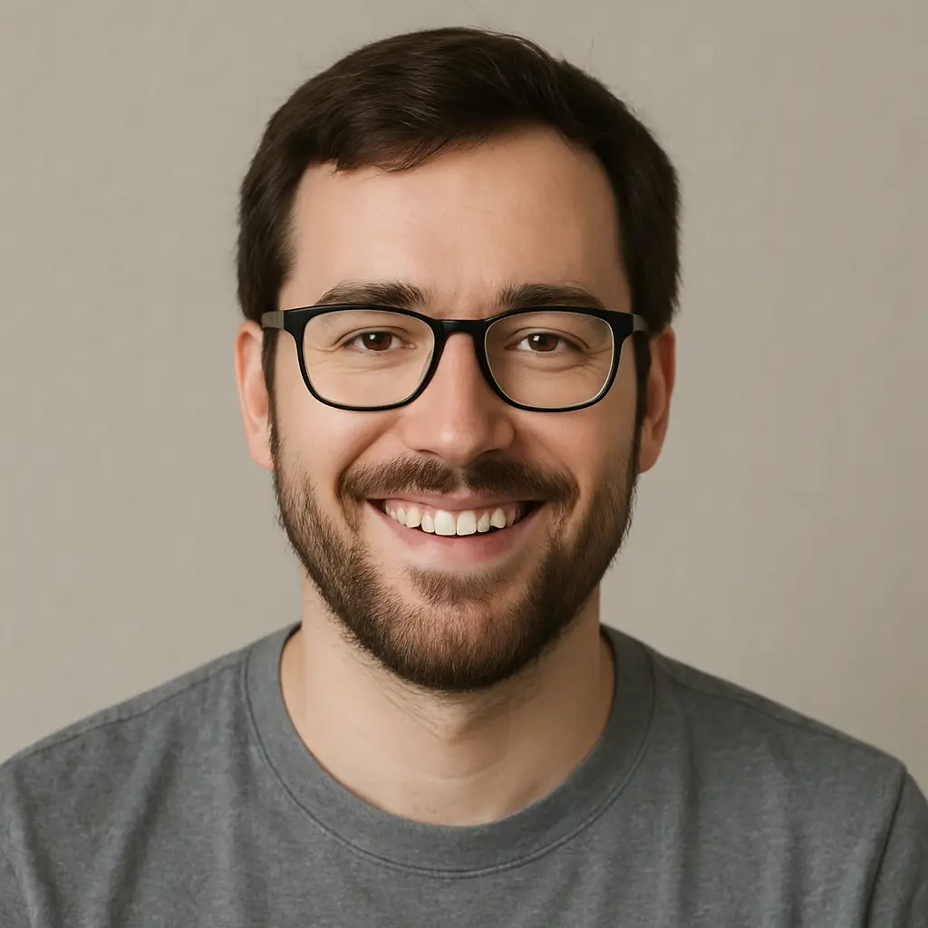 Professional headshot of smiling Henry founder of unlimiteddesignresources.com man with dark hair, beard, and black-framed glasses wearing gray t-shirt against neutral background